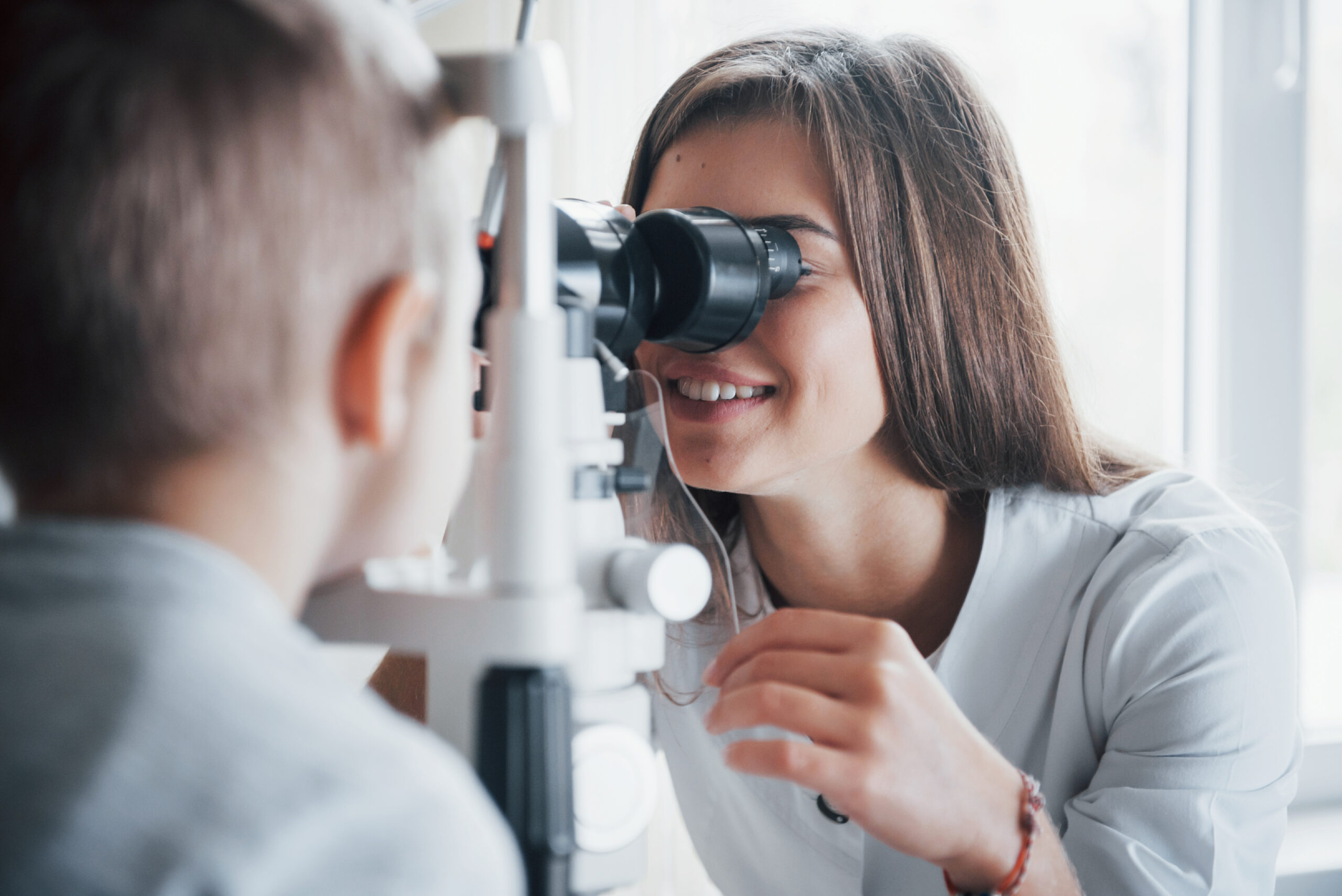 Close look. Little boy having test for his eyes with special optical apparatus by female doctor.